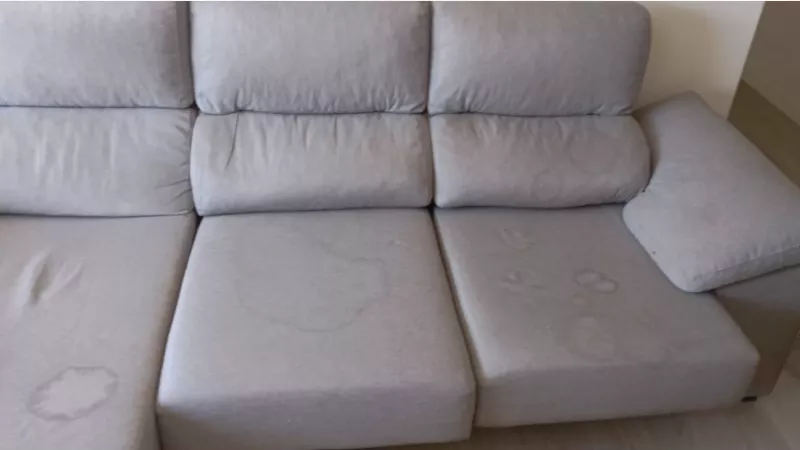 Sofá cinzento com auréolas e marcas visíveis em vários assentos