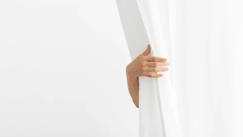 Mão a afastar um cortinado branco junto à janela